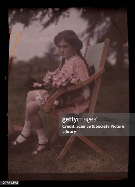 An autochrome of her daughter sitting in a garden chair holding a large bunch of freshly picked flowers, taken by Etheldreda Janet Laing. In the...