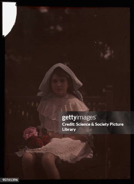 An autochrome of her daughter wearing a bonnet and lace dress, holding a bunch of freshly picked red and pink roses, taken by Etheldreda Janet Laing....