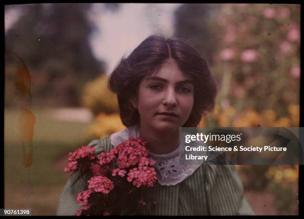 An autochrome of her daughter in a garden, holding a brightly coloured bunch of pink flowers, taken by Etheldreda Janet Laing. In the summer of 1908...