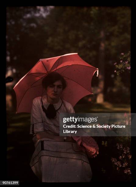 An autochrome of a young girl, daughter of the photographer, sitting in the shade in a garden, holding a parasol over her shoulder, taken by...