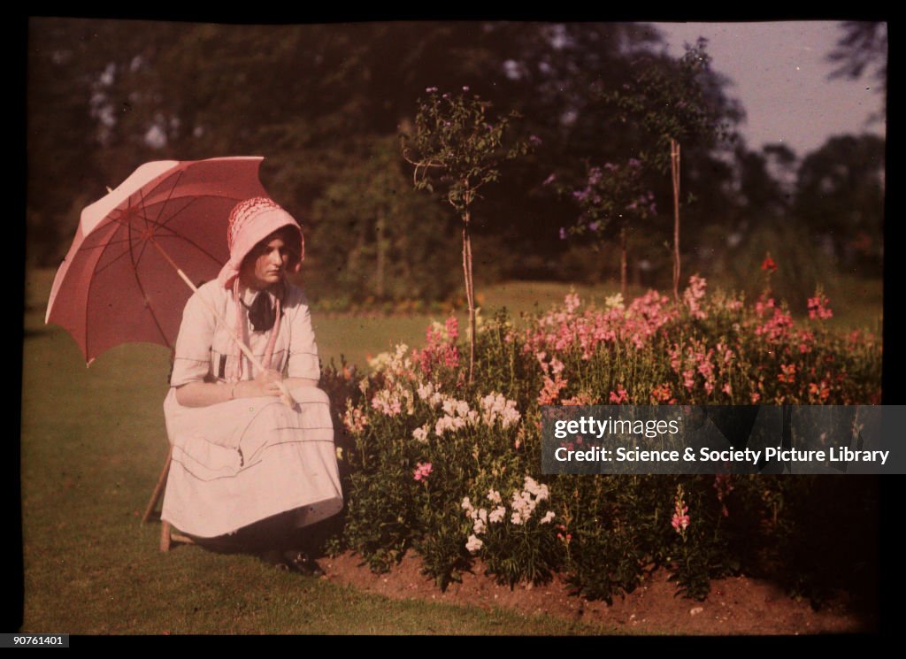 Girl with a parasol sitting by a flower bed, 1908.