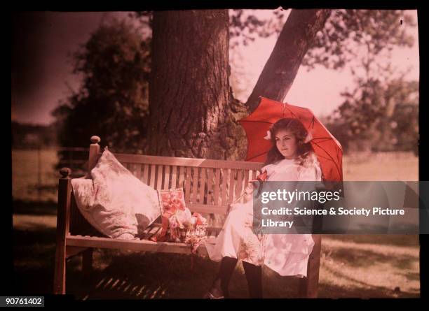 An autochrome of her daughter sitting under a tree, taken by Etheldreda Janet Laing. Next to her, a basket overflows with ribbons and thread as she...