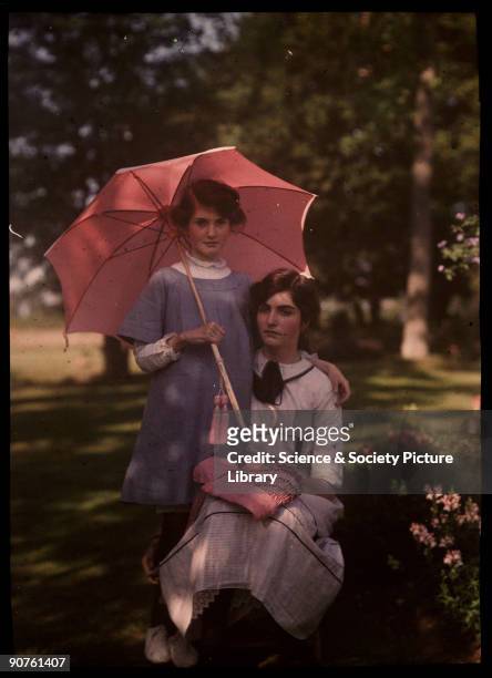 An autochrome of her daughters taken by Etheldreda Janet Laing. The younger girl stands beside her sister holding a pink parasol. The older girl...