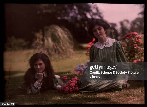 An autochrome of her daughters by Etheldreda Janet Laing. The two sisters, dressed in matching green-striped dresses, relax on the grass in this...