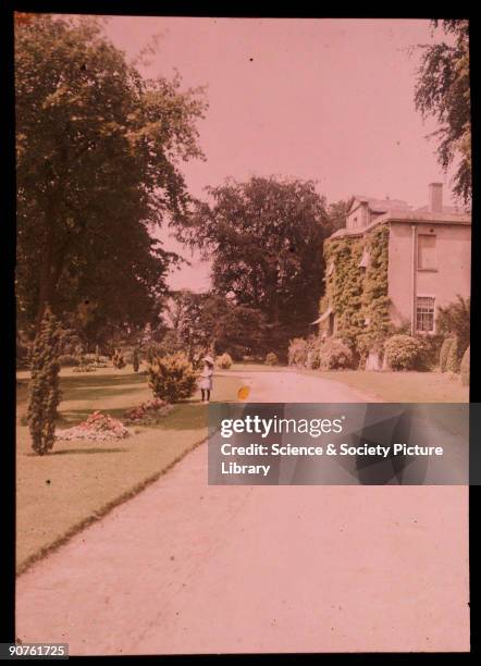 An autochrome of a large detached house and its garden and driveway, taken by Etheldreda Janet Laing in about 1910. A little girl in a white bonnet...