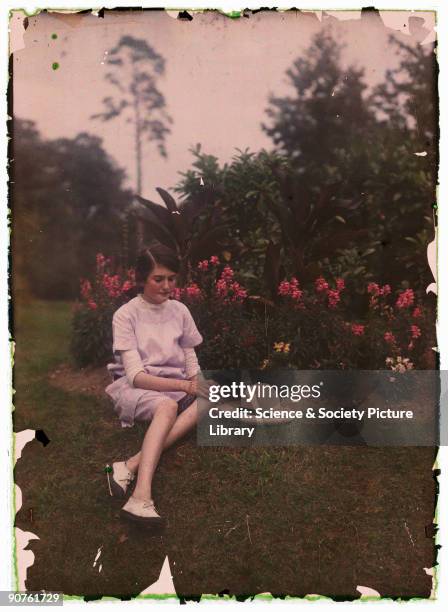 An autochrome of a young girl in a garden next to a flowerbed, taken by Etheldreda Janet Laing in about 1910. The young girl, her straw bonnet on the...