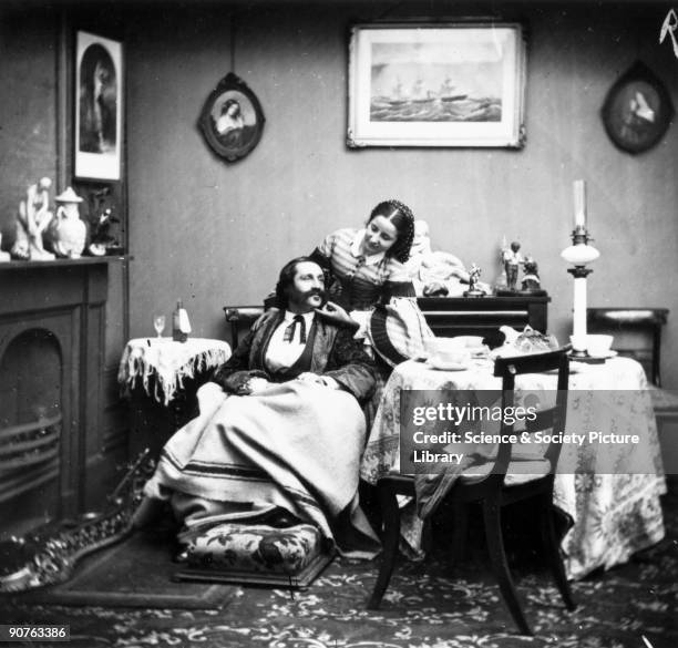 Victorian scene with a man wrapped in a blanket, a bottle of medicine on the table beside him. His wife bends over him solicitously.