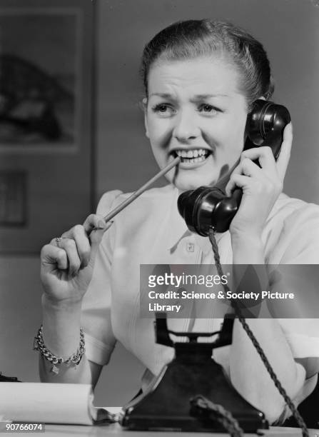 Photograph of a woman answering a telephone, chewing on a pencil, taken by Photographic Advertising Limited in 1955. Photographic Advertising Limited...