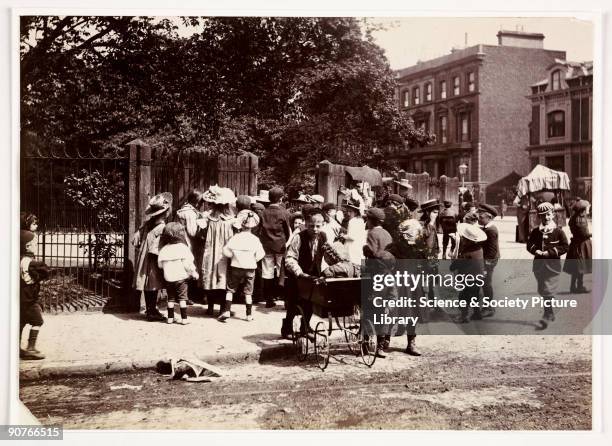 Photograph taken by Paul Martin in about 1905 of a busy streetscene. A crowd of children gather around a gateway to a London park. A boy in the...