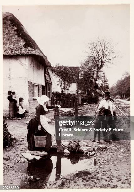 Photograph titled 'Village News', of villagers chatting whilst going about their daily business, taken by Colonel Joseph Gale in 1889. A man in work...