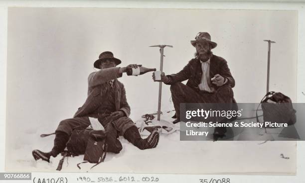 Snapshot photograph of two mountaineers sitting in the snow drinking a bottle of wine, taken by an unknown photographer in about 1910. Originally a...