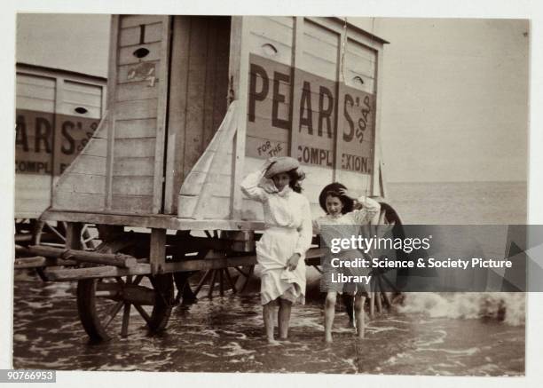 Snapshot photograph of a young woman and a girl at the seaside taken by an unknown photographer in about 1900. They hold onto their hats in the sea...