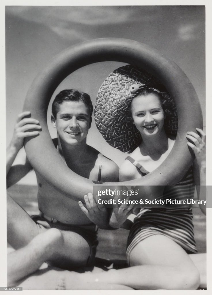 Man and woman looking through a rubber ring on beach, c 1935.