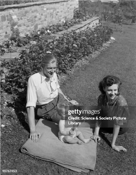 Photograph of a young couple and their baby sitting in a sunny garden, taken by Photographic Advertising Limited in 1948. This image was used for...