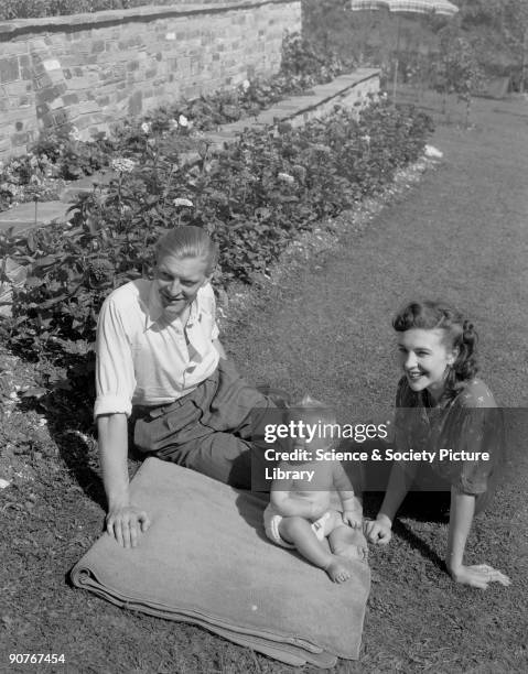 Photograph of a young couple and their baby sitting in a sunny garden, taken by Photographic Advertising Limited in 1948. Photographic Advertising...