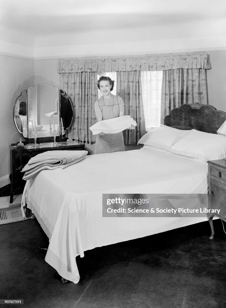 Woman folding laundry in a bedroom, c 1950.