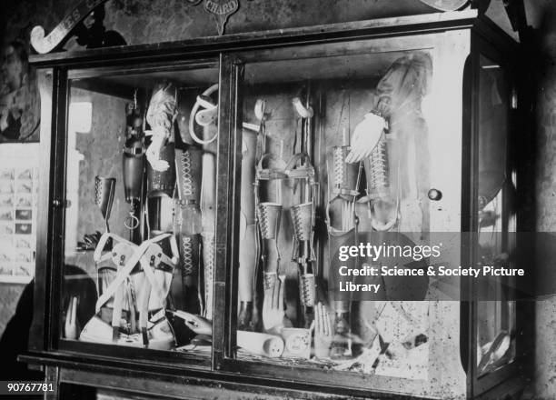 Photograph of a glass cabinet containing artificial arms, legs, hands and orthopaedic corsets. All of the items were manufactured by James Gillingham...