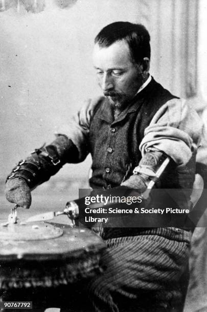 Studio photograph of a seated man eating with the aid of a pair of artificial arms. The arms were manufactured by James Gillingham , a boot- and...