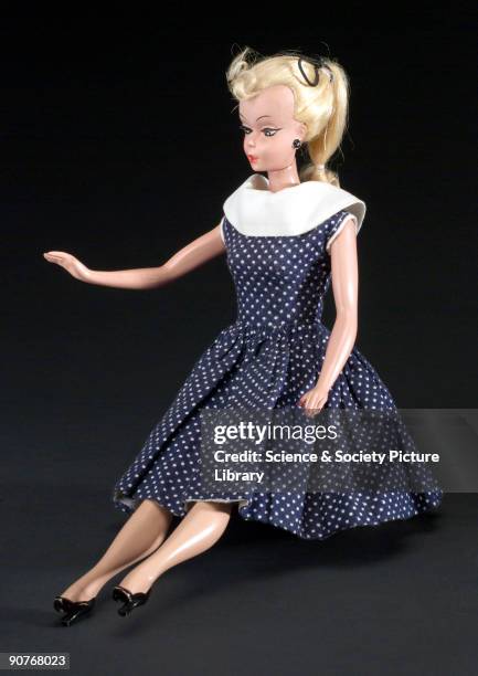 Doll made of all rigid plastic with jointed limbs, blond hair in a ponytail with a front curl, painted black earrings and heels. The doll is dressed...