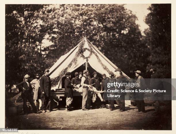 Albumen print of a Union Army hospital tent on the battlefield at Gettysburg. An injured man lies on a table while the surgeon stands nearby with a...