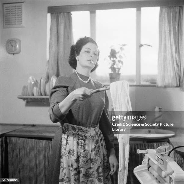 Woman doing her washing in a kitchen, 1955. She is about to remove excess water by wringing the washing through an Acme mangle. This is a production...