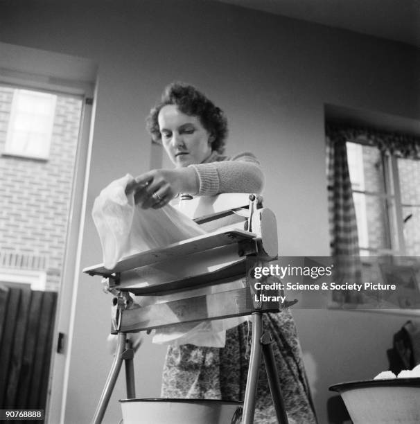 Woman using a mangle in her kitchen, 1955. She is about to remove excess water by wringing the washing through an Acme mangle. This is a production...