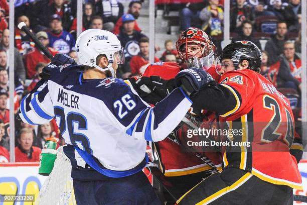 Mike Smith and Travis Hamonic of the Calgary Flames shove Blake Wheeler of the Winnipeg Jets during an NHL game at Scotiabank Saddledome on January...