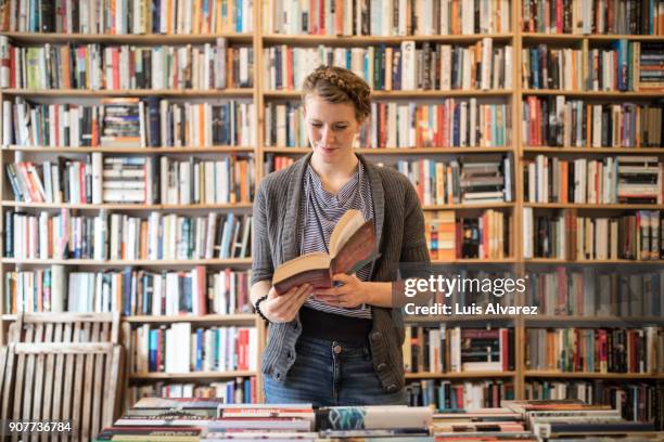 beautiful young female customer reading book at bookstore - bookshelf foto e immagini stock