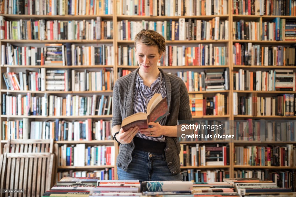 Beautiful young female customer reading book at bookstore