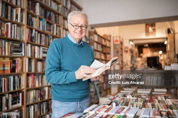 smiling senior male customer reading book at bookstore - sfogliare libro foto e immagini stock