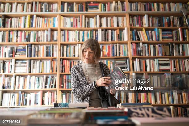 senior woman with book standing against bookshelf - buchhandlung stock-fotos und bilder