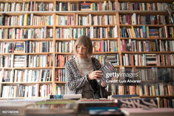 senior woman with book standing against bookshelf - libreria fotografías e imágenes de stock