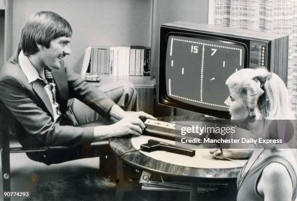 Photograph showing Liverpool FC and England footballer Steve Heighway and a woman playing the computer tennis game Pong on the Videomaster games...