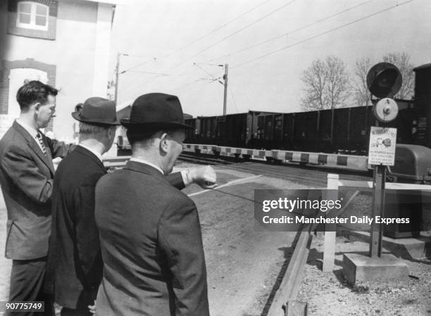 Men look at their watches as a freight train passes through a level crossing.