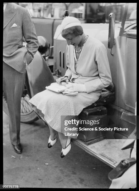 Charly Caracciola, wife of German racing driver Rudolf Caracciola, sitting on car running board with notebook and stopwatches. In 1933, Caracciola...