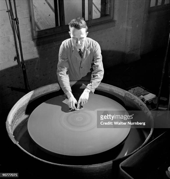 Using a huge spherical polishing disc, a Taylor Hobson worker finishes a camera lens. Innovation and consistent technical quality lead to...