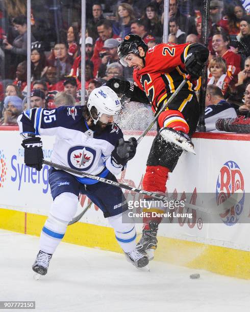 Travis Hamonic of the Calgary Flames gets checked by Mathieu Perreault of the Winnipeg Jets during an NHL game at Scotiabank Saddledome on January...