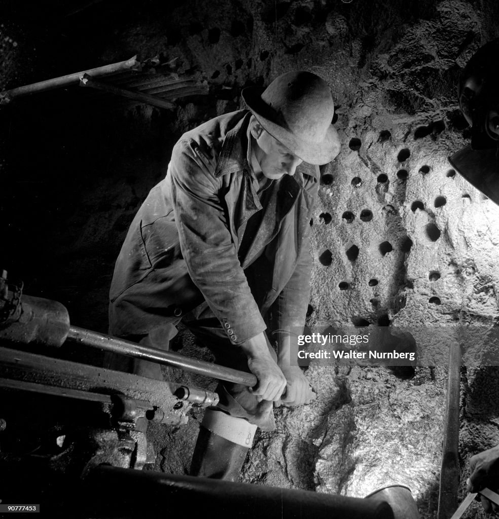 A miner guides a drill in to a rock underground, Holman Brothers, 1948.