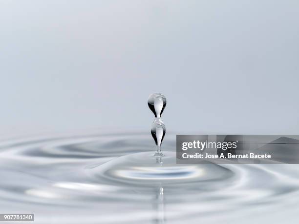 group of drops on line suspended in the air, falling down on a water surface that forms figures and abstract forms, on a gray background - sinus stockfoto's en -beelden