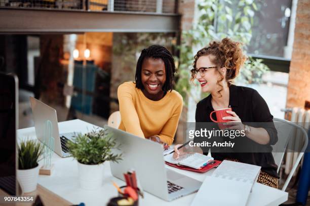 twee vrouwelijke ondernemers werken op de computer in kantoor - werkplek stockfoto's en -beelden