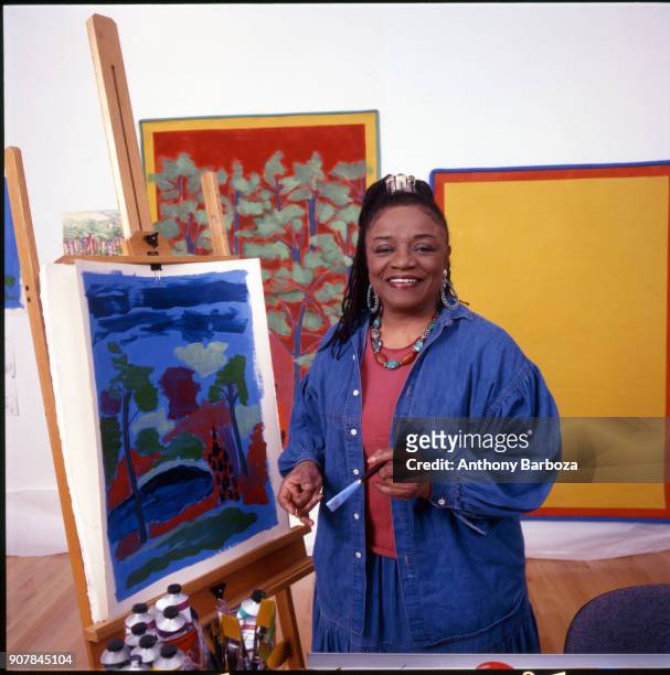 Portrait of American artist Faith Ringgold as she poses in front of one of her paintings in her studio, New York, New York, 1999.