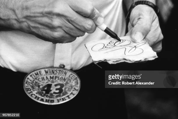 Driver Richard Petty signs his autograph on a piece of cardboad prior to the start of the 1984 Daytona 500 NASCAR race at Daytona International...