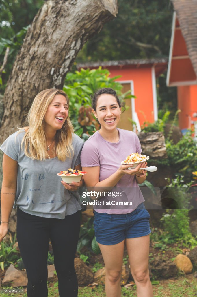 Young women holding smoothie bowls with fresh tropical fruit outdoors