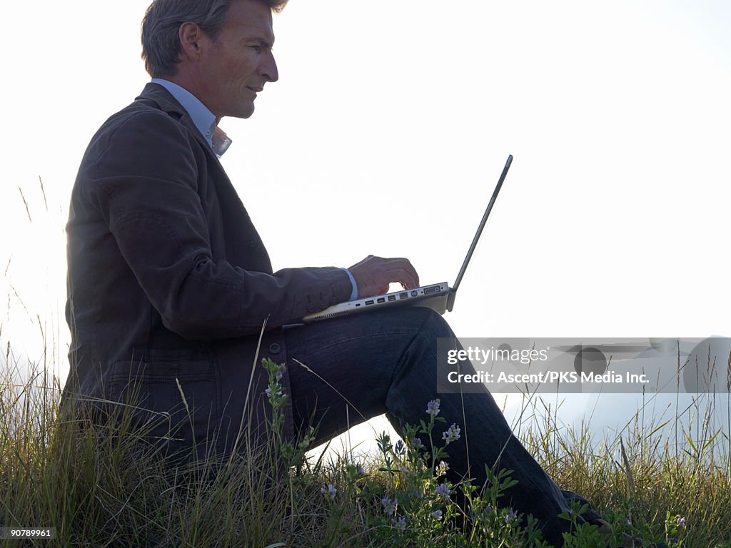 Man works on lap top computer, on ridge crest