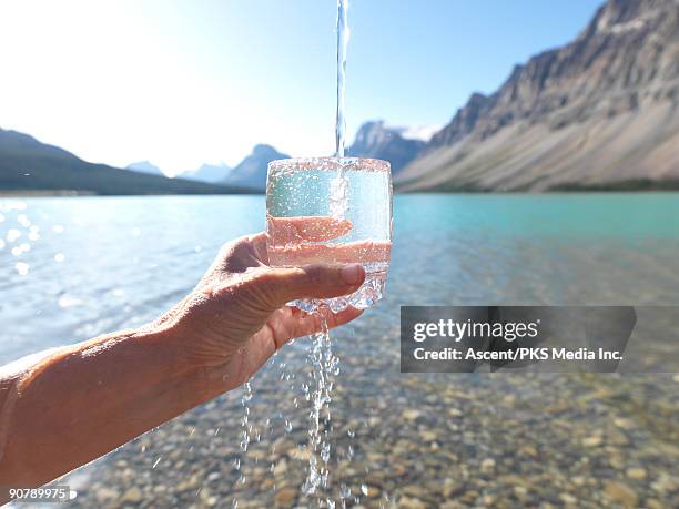 hand holds glass with water pouring in,  mtn lake - overflowing glass stockfoto's en -beelden