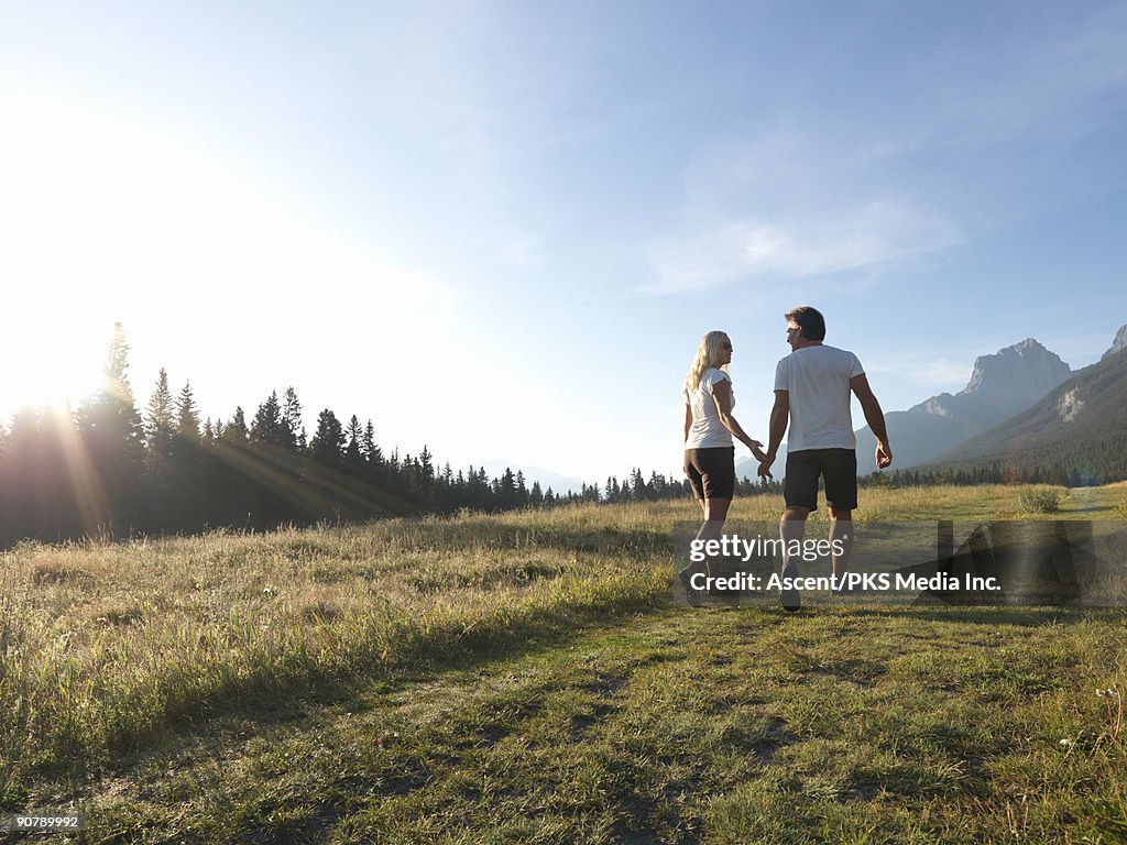 Couple walk through mountain meadow, conversing