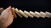 Management intervention or decision suggested by businesswoman hand stopping the negative continuous effects, with wooden blocks as dominoes on black background