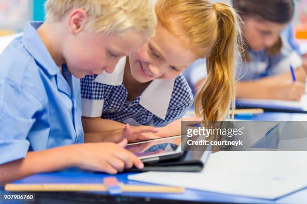 boy and girl students working on a digital tablet - school uniform stock pictures, royalty-free photos & images