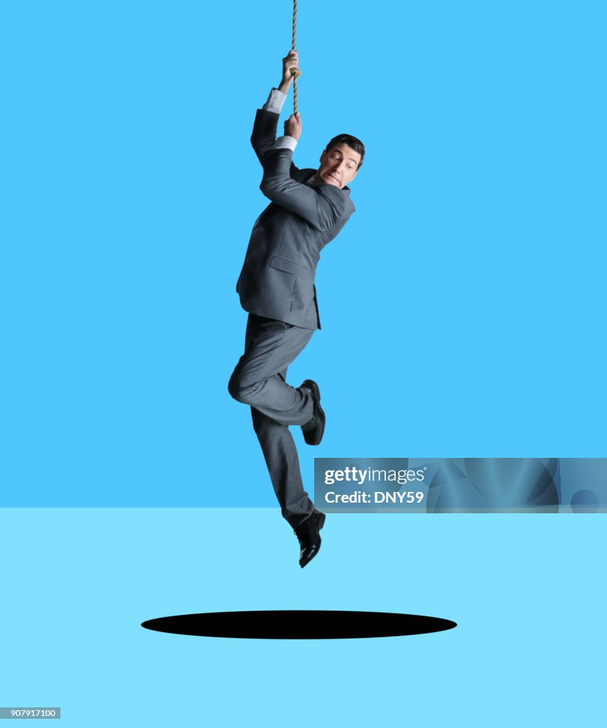 Businessman Hanging From Rope Looks Down At Hole