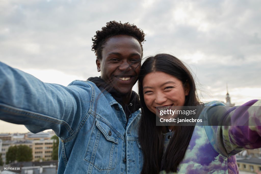 Multi ethnic couple hugging on the rooftop. Making selfie